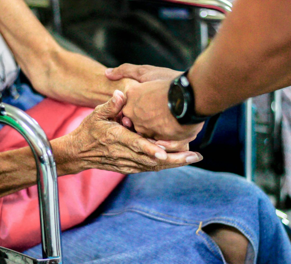 A volunteer holding the hands of an older woman in a wheelchair