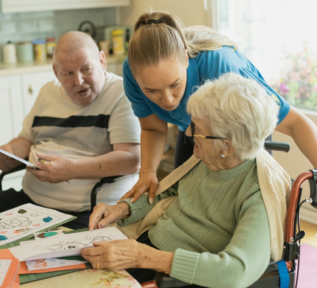 A volunteer helping an older woman with a craft at her kitchen table
